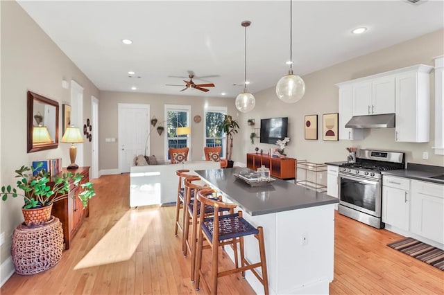 kitchen with decorative light fixtures, stainless steel gas stove, a breakfast bar area, white cabinets, and light wood-type flooring