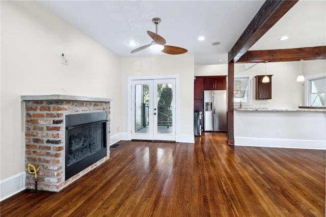 unfurnished living room with beamed ceiling, french doors, ceiling fan, a brick fireplace, and dark hardwood / wood-style floors