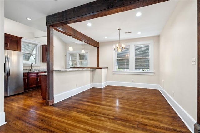 interior space featuring decorative light fixtures, beamed ceiling, kitchen peninsula, stainless steel fridge, and dark wood-type flooring