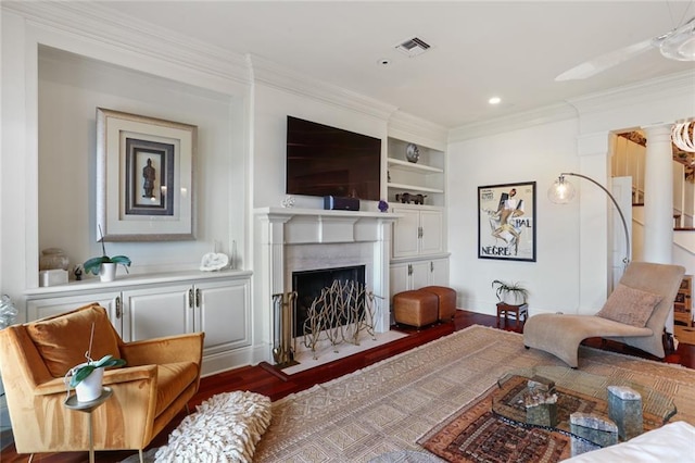 living room with dark wood-type flooring, ornamental molding, a premium fireplace, and built in features