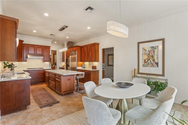 kitchen featuring sink, hanging light fixtures, ornamental molding, stainless steel fridge, and an island with sink