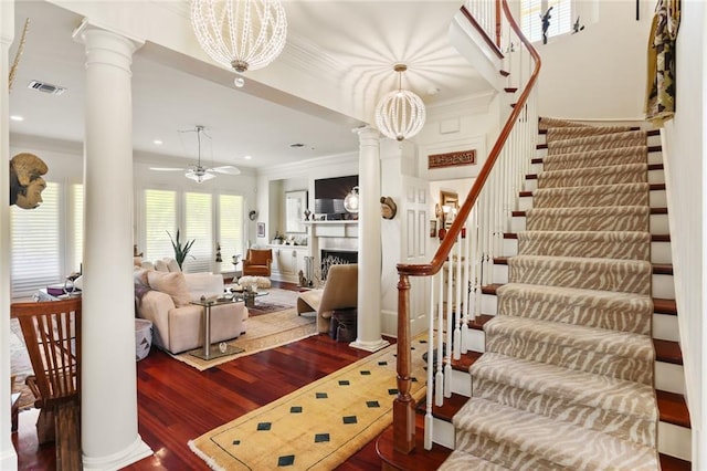 living room featuring dark wood-type flooring, ceiling fan, crown molding, and ornate columns