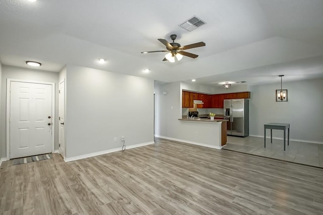 unfurnished living room featuring ceiling fan with notable chandelier and light hardwood / wood-style floors