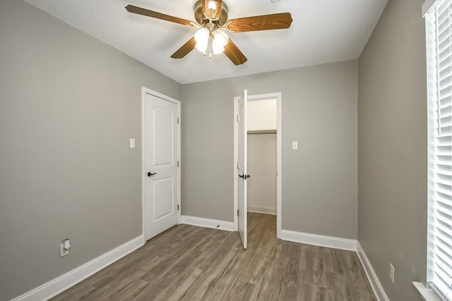 unfurnished bedroom with ceiling fan, a walk in closet, hardwood / wood-style floors, and a closet