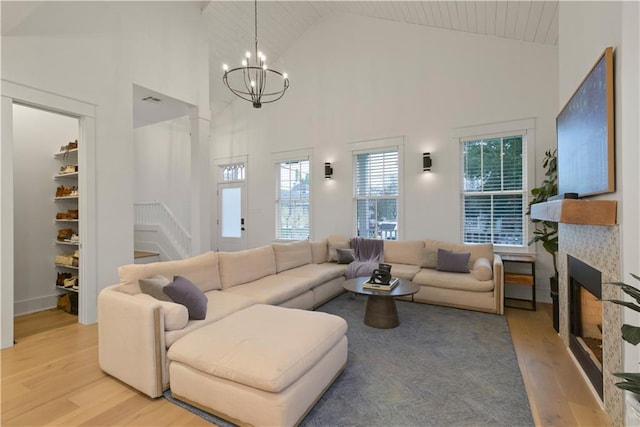 living room with high vaulted ceiling, a tiled fireplace, an inviting chandelier, and light hardwood / wood-style flooring