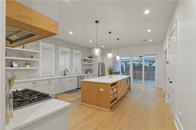 kitchen featuring decorative light fixtures, white cabinetry, light hardwood / wood-style flooring, a kitchen island, and appliances with stainless steel finishes