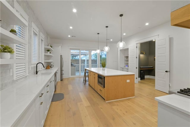 kitchen featuring white cabinets, stainless steel refrigerator, light wood-type flooring, a center island, and sink