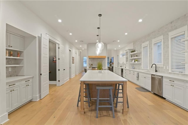 kitchen with decorative light fixtures, a center island, white cabinetry, dishwasher, and a kitchen bar