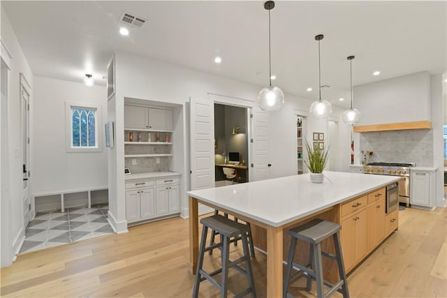 kitchen with a breakfast bar area, stainless steel range, decorative backsplash, a spacious island, and white cabinetry