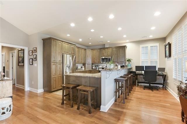 kitchen with light hardwood / wood-style floors, a breakfast bar, stainless steel appliances, and light stone countertops