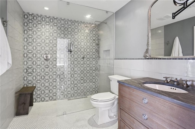 bathroom featuring toilet, vanity, tile patterned floors, tile walls, and a tile shower