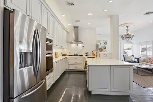 kitchen featuring white cabinets, an inviting chandelier, kitchen peninsula, exhaust hood, and appliances with stainless steel finishes