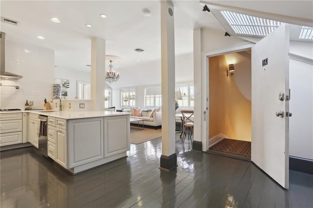 kitchen featuring kitchen peninsula, wall chimney exhaust hood, dishwasher, dark hardwood / wood-style floors, and a notable chandelier