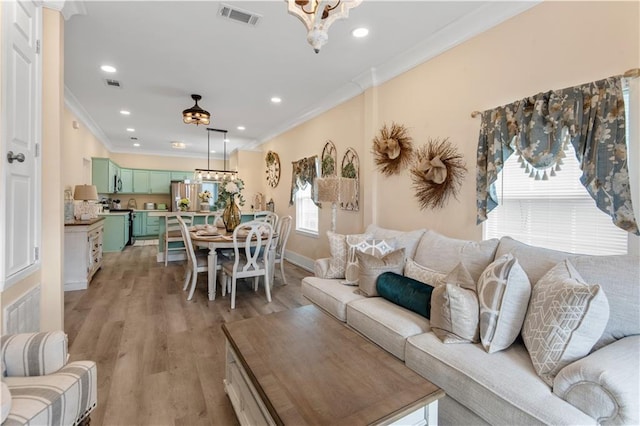 living room with ornamental molding, an inviting chandelier, and light hardwood / wood-style flooring