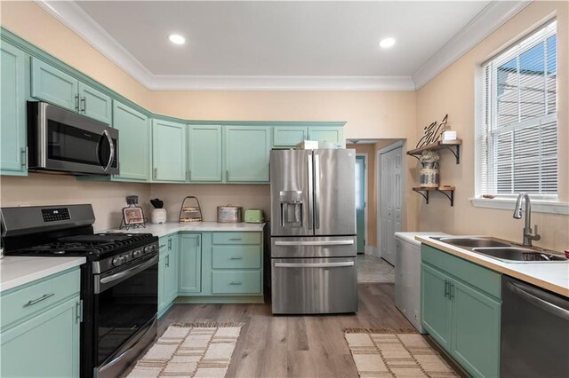 kitchen featuring stainless steel appliances, sink, green cabinetry, ornamental molding, and light wood-type flooring