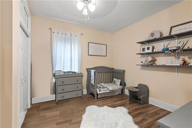 bedroom featuring ceiling fan, a closet, a crib, and dark hardwood / wood-style floors