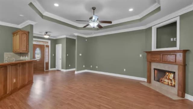 unfurnished living room featuring a high end fireplace, light hardwood / wood-style floors, ornamental molding, ceiling fan, and a tray ceiling