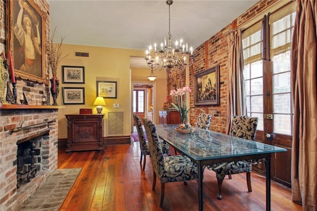 dining room featuring a brick fireplace, dark wood-type flooring, french doors, and a notable chandelier