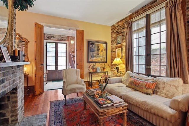 living room with french doors, a brick fireplace, brick wall, and hardwood / wood-style flooring