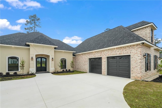 french country inspired facade with an attached garage, french doors, driveway, and roof with shingles