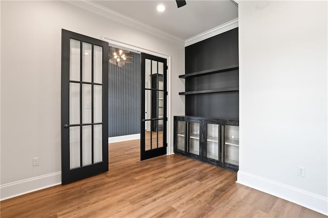 unfurnished room featuring an inviting chandelier, french doors, light hardwood / wood-style floors, built in shelves, and crown molding