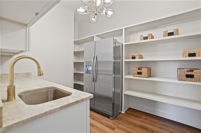 kitchen with sink, a notable chandelier, wood-type flooring, light stone countertops, and stainless steel fridge with ice dispenser