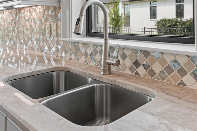 interior details with sink, light stone counters, and decorative backsplash