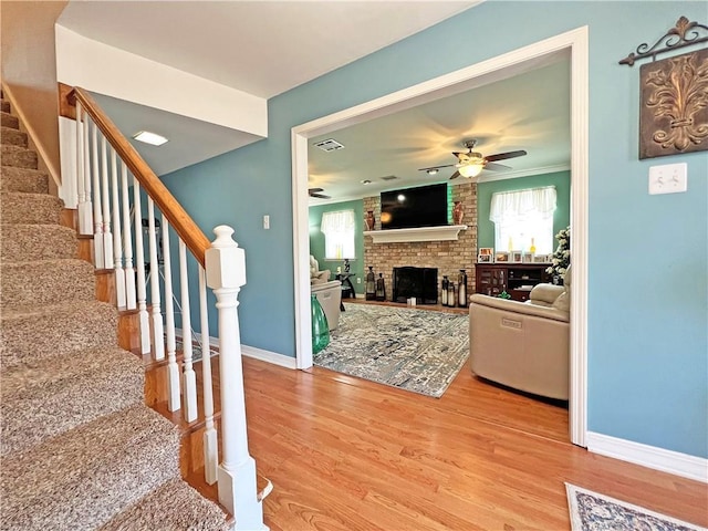 living room with ceiling fan, light hardwood / wood-style floors, a brick fireplace, and crown molding