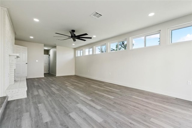 unfurnished living room with a brick fireplace, light wood-type flooring, and ceiling fan