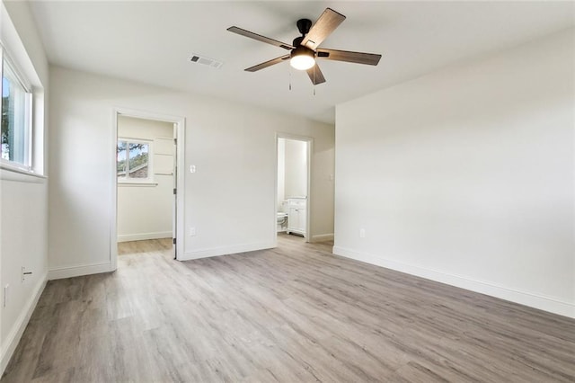 unfurnished bedroom with a spacious closet, a closet, connected bathroom, light wood-type flooring, and ceiling fan