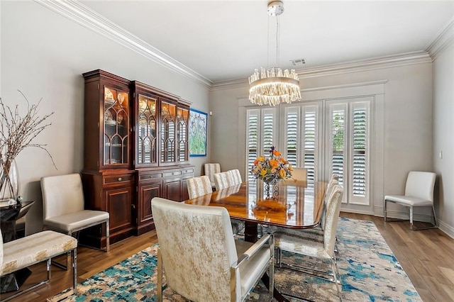 dining space with ornamental molding, an inviting chandelier, and light wood-type flooring