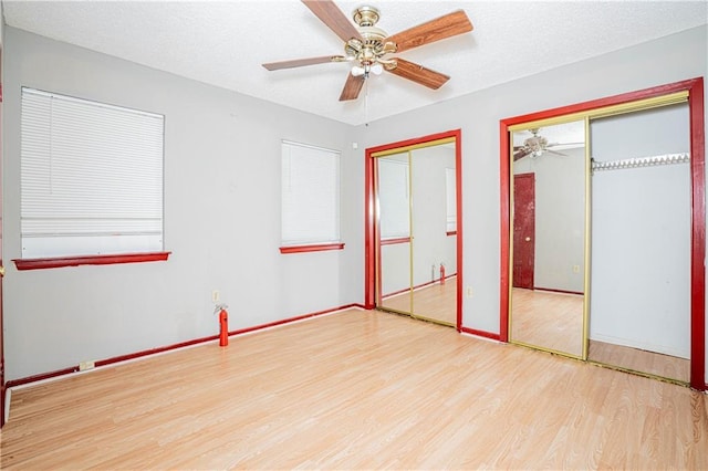 unfurnished bedroom featuring a textured ceiling, ceiling fan, light hardwood / wood-style floors, and multiple closets