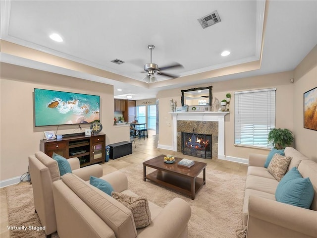 living room featuring a raised ceiling, a fireplace, ceiling fan, and crown molding