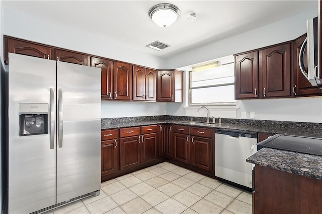 kitchen with stainless steel appliances, dark stone counters, light tile patterned floors, and sink