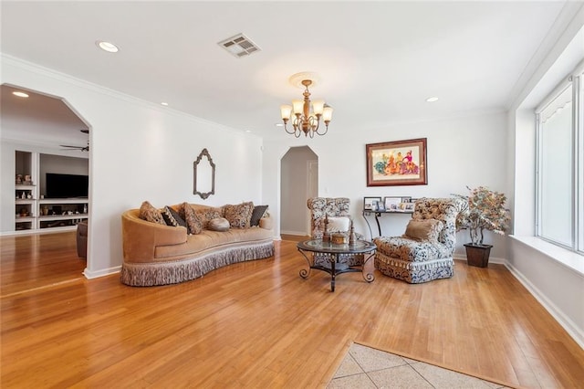 living room featuring ceiling fan with notable chandelier, wood-type flooring, built in shelves, and ornamental molding