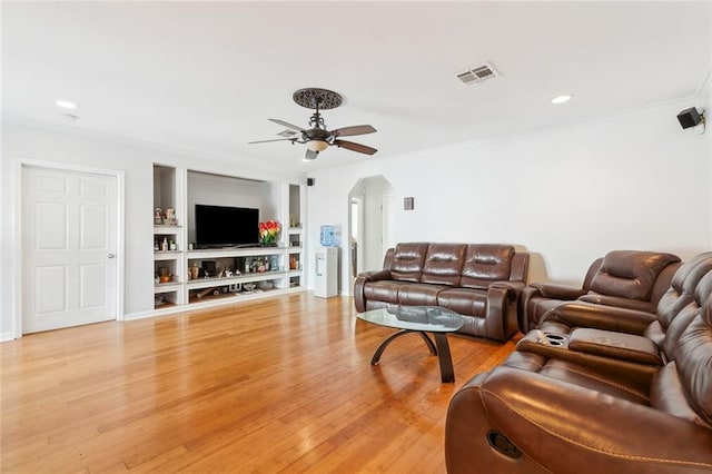 living room with light wood-type flooring, ceiling fan, crown molding, and built in shelves