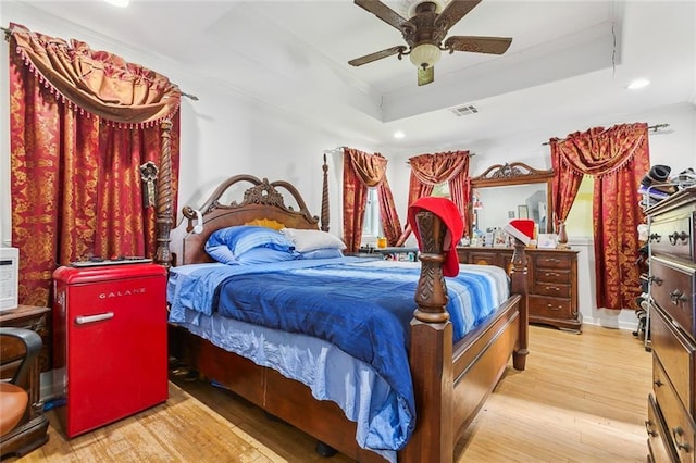 bedroom with ceiling fan, a tray ceiling, ornamental molding, and light hardwood / wood-style floors