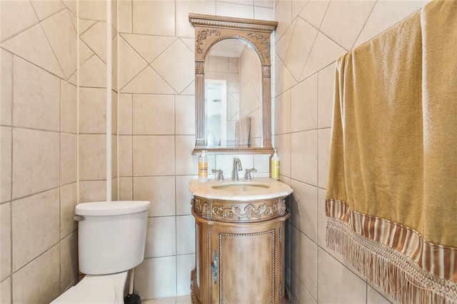 bathroom with toilet, vanity, and tile walls