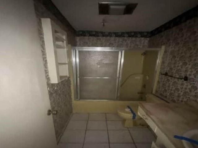 bathroom featuring toilet, a shower with door, and tile patterned flooring