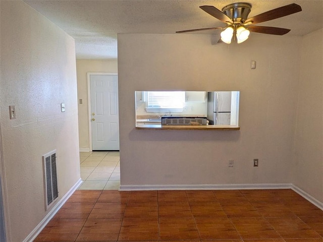 interior space with tile patterned flooring, visible vents, ceiling fan, baseboards, and a textured ceiling