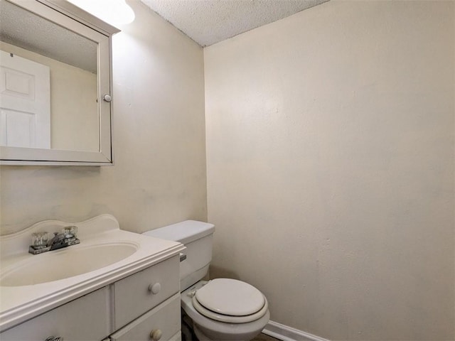 half bath featuring baseboards, toilet, vanity, and a textured ceiling