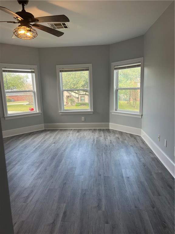 spare room featuring baseboards, visible vents, ceiling fan, and dark wood-type flooring