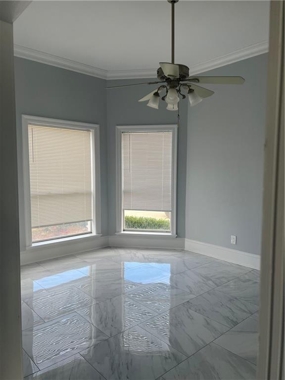 empty room with a ceiling fan, marble finish floor, crown molding, and baseboards