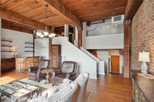 living room featuring light hardwood / wood-style floors, beamed ceiling, an inviting chandelier, brick wall, and wooden ceiling