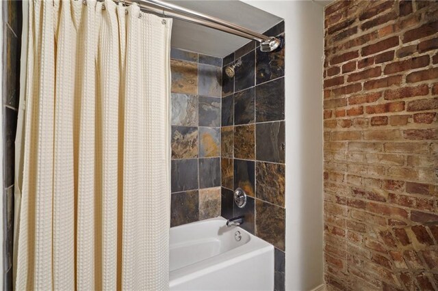 bathroom with shower / bath combo and brick wall