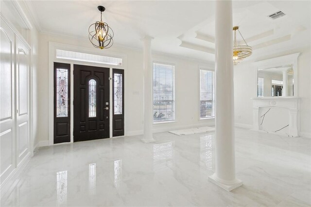 foyer entrance featuring a raised ceiling, ornamental molding, a notable chandelier, and decorative columns