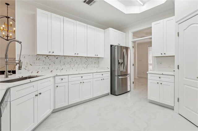 kitchen with hanging light fixtures, stainless steel fridge, crown molding, white cabinets, and sink