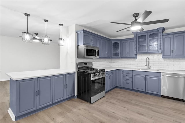 kitchen with pendant lighting, sink, stainless steel appliances, and light wood-type flooring