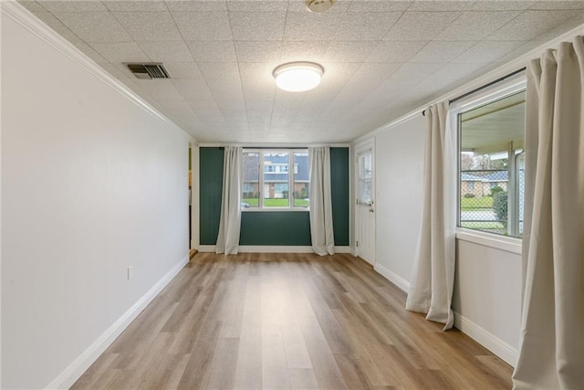 spare room featuring a healthy amount of sunlight, crown molding, and light hardwood / wood-style flooring