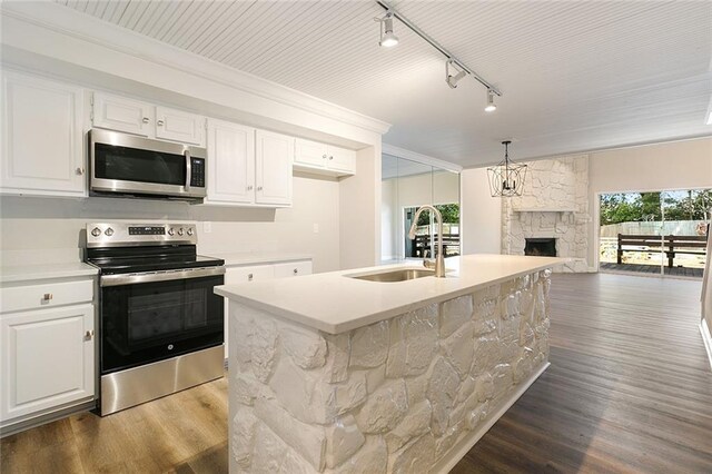 kitchen featuring white cabinetry, stainless steel appliances, a stone fireplace, sink, and a kitchen island with sink